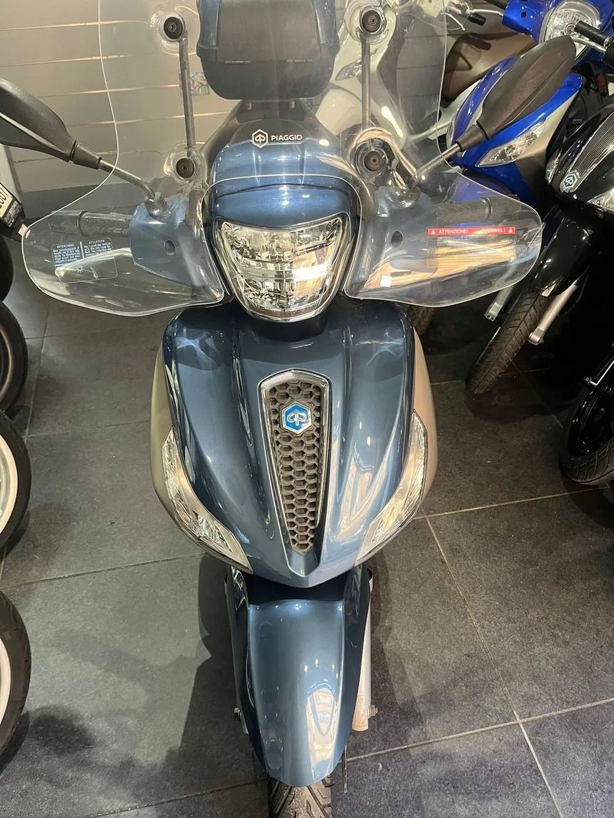 Scooter Piaggio blu con parabrezza, in uno showroom.