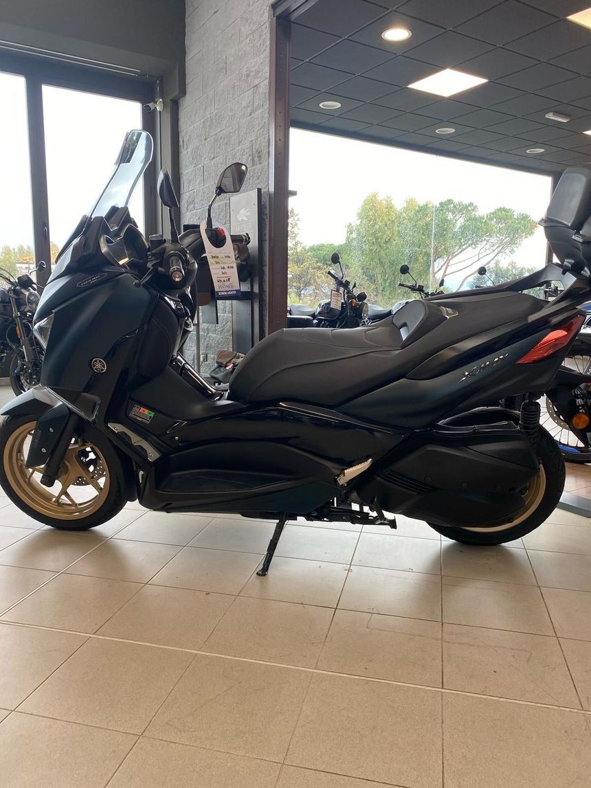 Scooter Yamaha X-MAX nero con ruote dorate parcheggiato al chiuso.