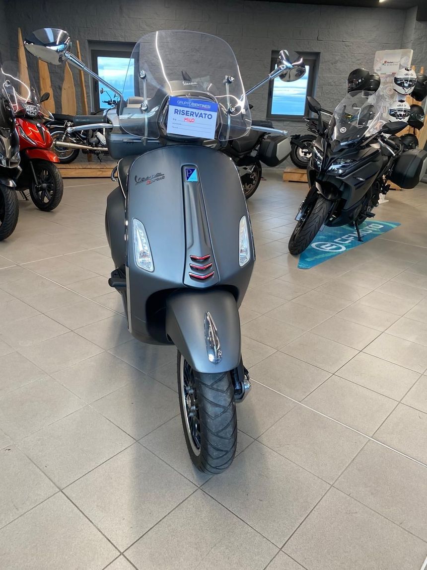 Scooter Vespa grigio con parabrezza esposto in uno showroom.