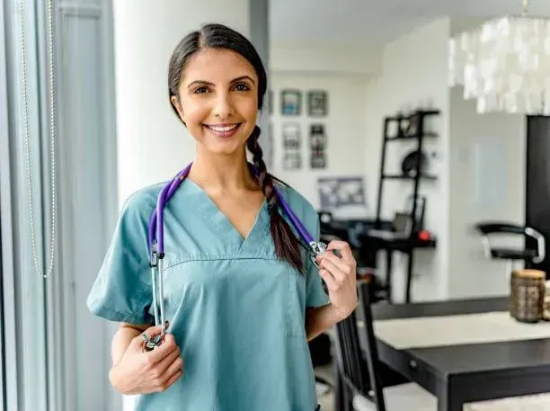 A nurse is standing in a living room holding a stethoscope around her neck.