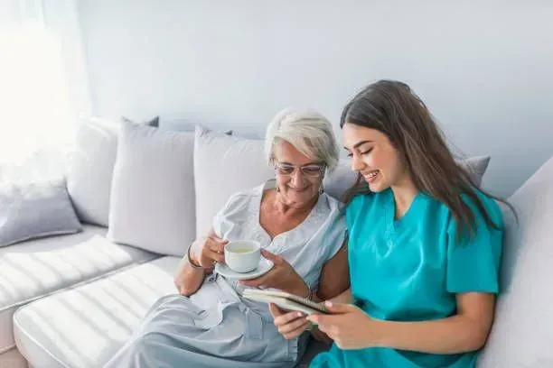 A nurse is sitting next to an elderly woman on a couch.