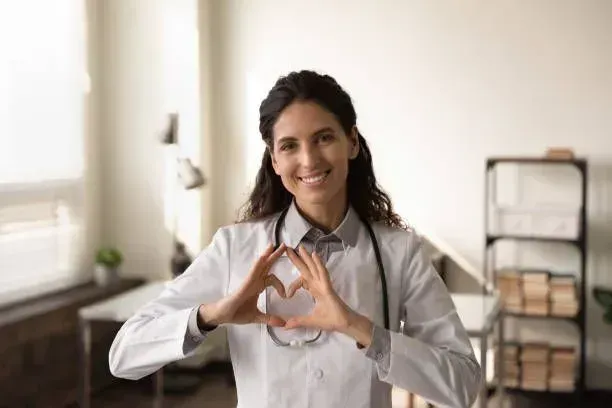 A female doctor is making a heart shape with her hands.