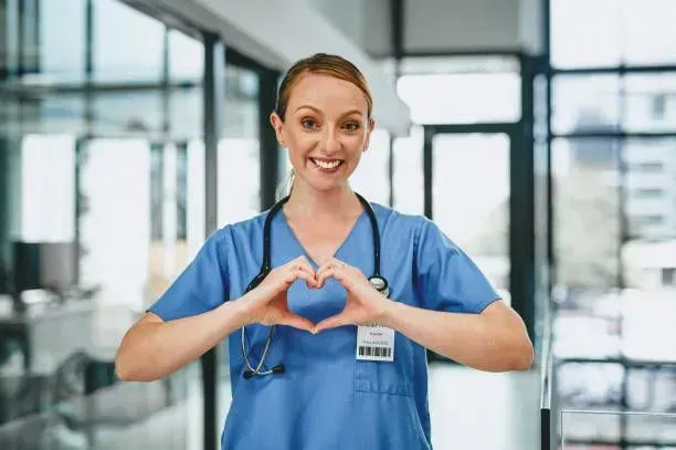 A nurse is making a heart shape with her hands in a hospital.