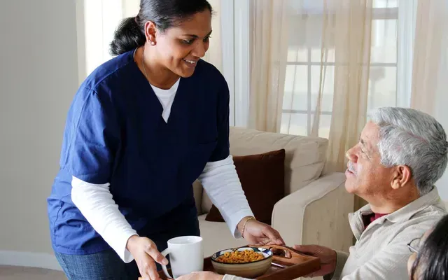 A nurse is serving food to an elderly woman in a living room.