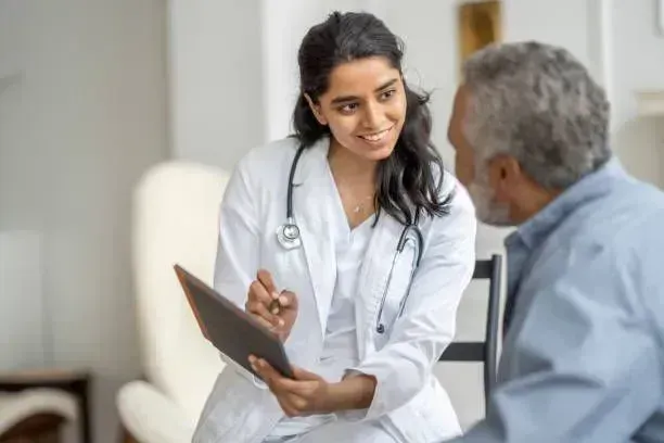 A female doctor is talking to an older man while holding a tablet.