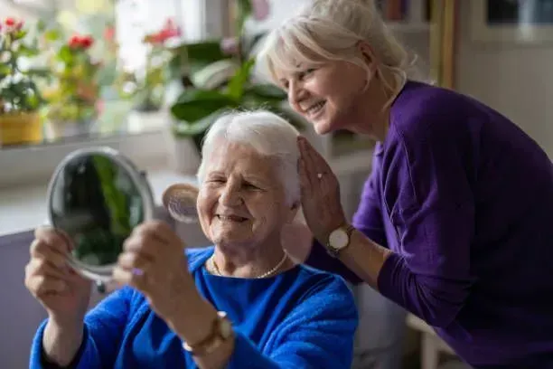 An elderly woman is looking at her hair in a mirror.
