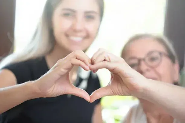 A young woman and an older woman are making a heart shape with their hands.