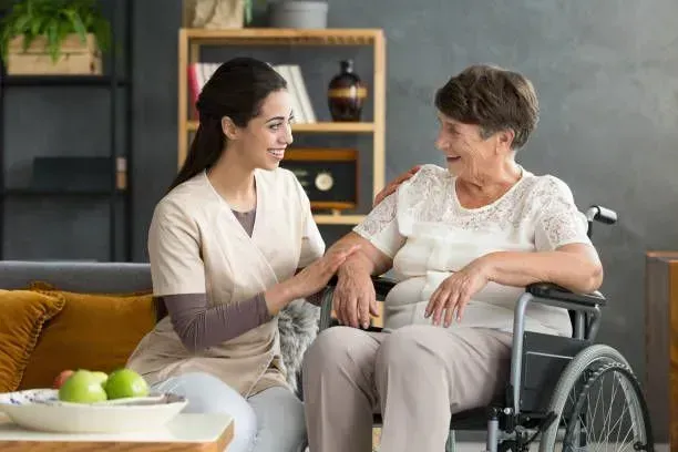 A nurse is sitting on a couch next to an elderly woman in a wheelchair.