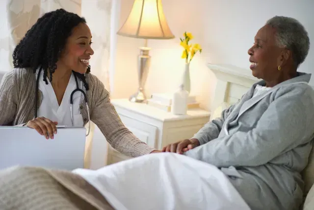 A nurse is talking to an elderly woman in a hospital bed.