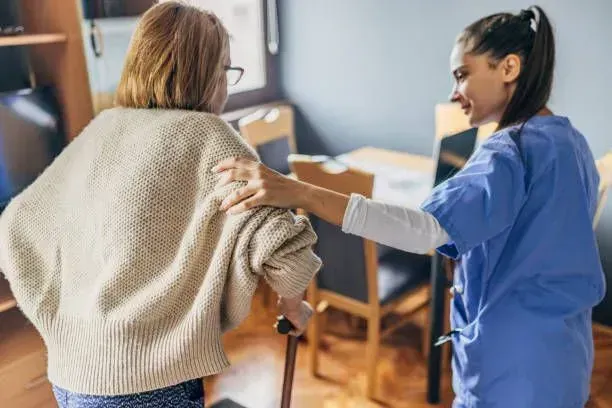 A nurse is helping an elderly woman walk with a cane.