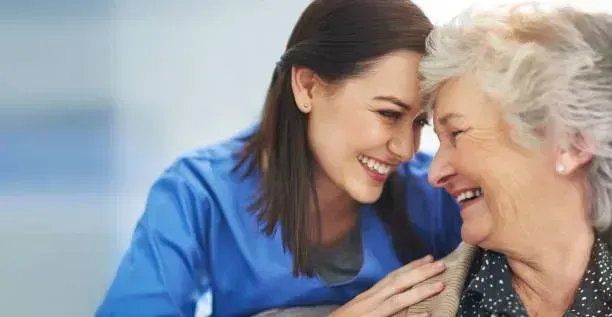 A nurse is talking to an elderly woman and smiling.