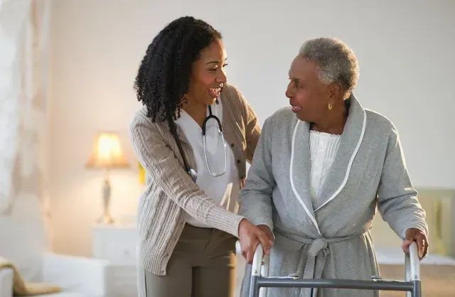 A nurse is helping an elderly woman with a walker.