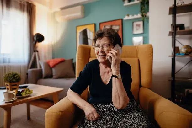 An elderly woman is sitting in a chair talking on a cell phone.