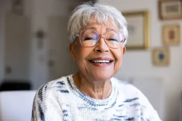 An elderly woman wearing glasses is smiling for the camera.