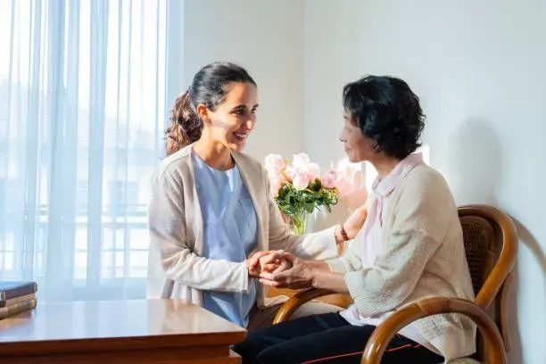 A woman is holding the hand of an older woman while sitting at a table.