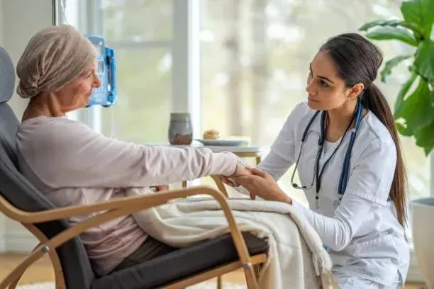 A nurse is holding the hand of an elderly woman in a chair.
