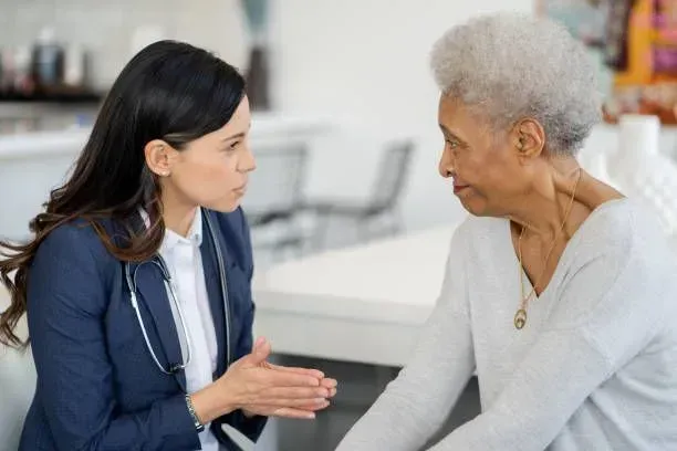 A woman is talking to an older woman who is sitting on a chair.
