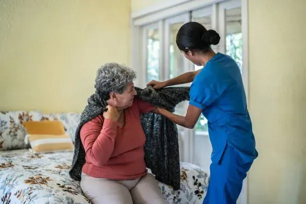 A nurse is helping an elderly woman get dressed on a bed.