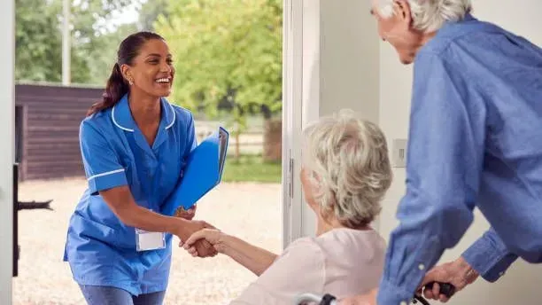 A nurse is shaking hands with an elderly woman in a wheelchair.