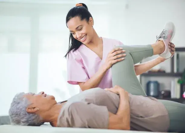 A nurse is helping an elderly woman stretch her leg.