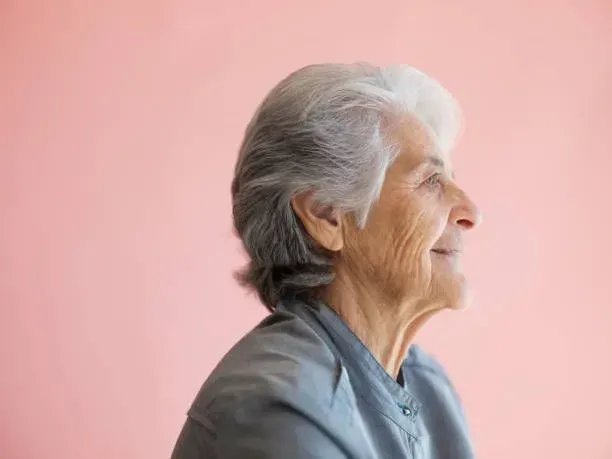 A close up of an elderly woman 's face on a pink background.