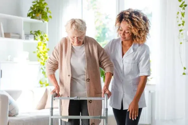 A nurse is helping an elderly woman walk with a walker.