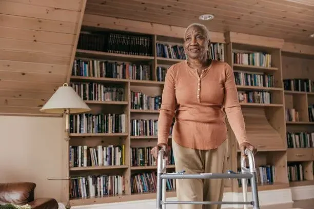 An elderly woman is using a walker in a living room.
