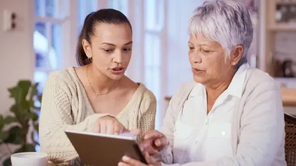A young woman is teaching an older woman how to use a tablet computer.