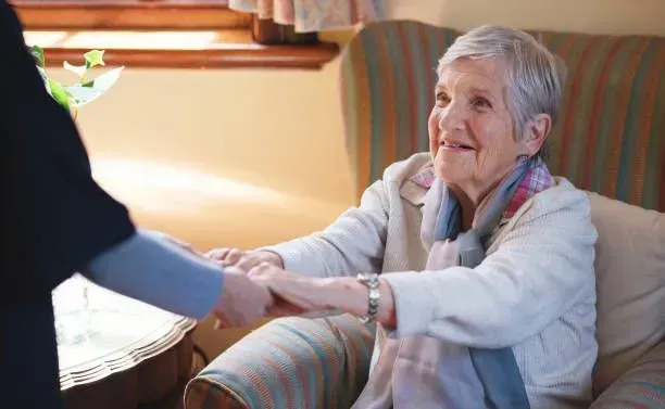 An elderly woman is sitting on a couch holding a nurse 's hand.