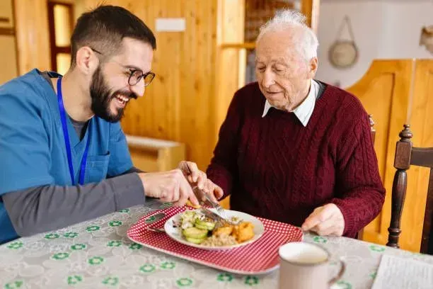 A man is feeding an elderly man a meal at a table.