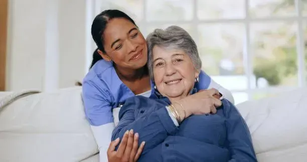 A nurse is hugging an elderly woman on a couch.