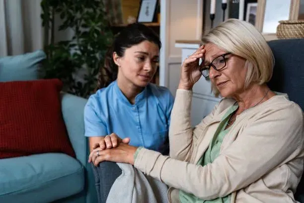 A nurse is comforting an elderly woman who is sitting in a chair.