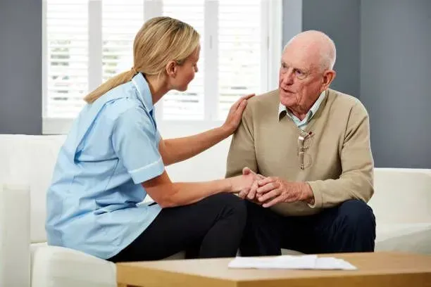A nurse is comforting an elderly man while sitting on a couch.