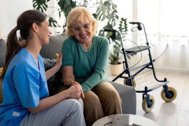 A nurse is talking to an elderly woman sitting on a couch.