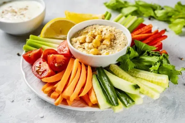 A plate of vegetables and a bowl of hummus on a table.