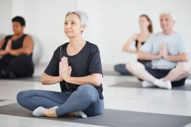 A group of people are sitting on yoga mats in a yoga class.