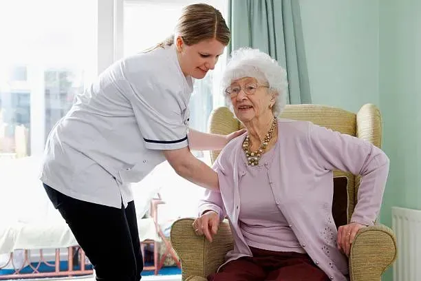 A nurse is helping an elderly woman sit in a chair.