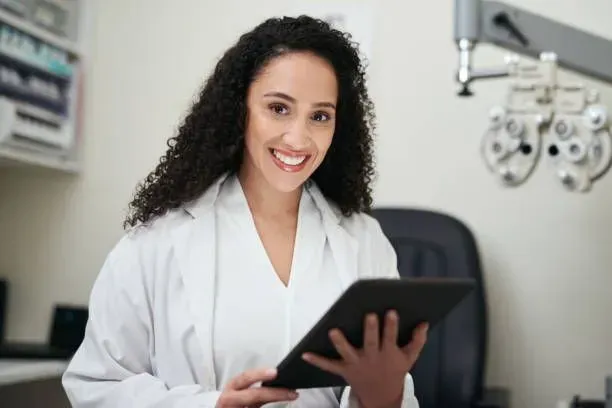 A woman in a lab coat is holding a tablet and smiling.