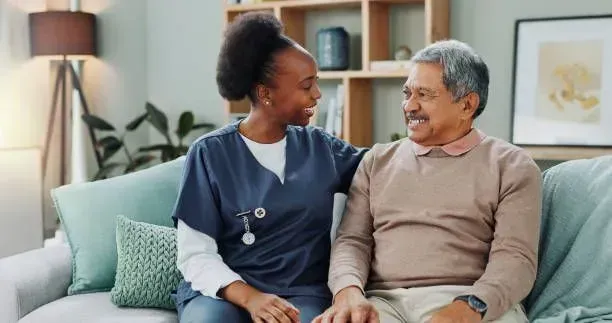 A nurse is sitting next to an elderly man on a couch.