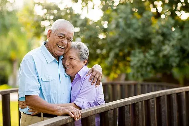 An elderly couple is standing on a wooden bridge.
