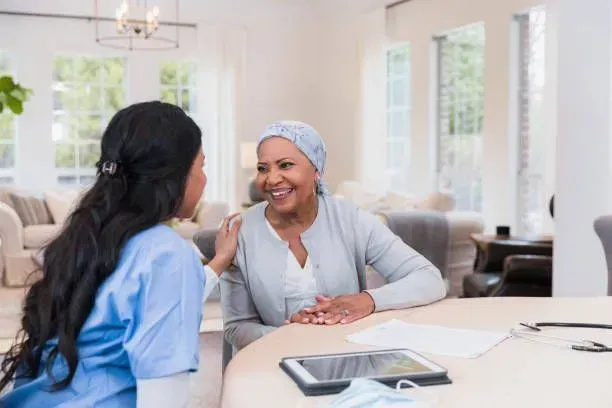 A nurse is talking to an older woman with cancer while sitting at a table.