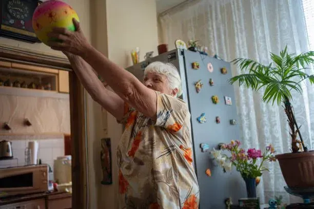 An elderly woman is playing with a ball in a kitchen.