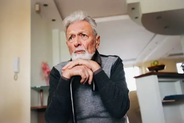 An elderly man with a beard is sitting in a chair with his hands folded.