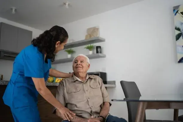 An elderly man is sitting in a chair with a nurse standing next to him.