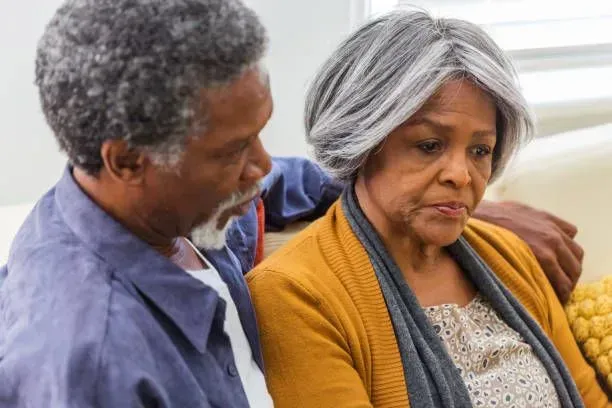 An elderly couple is sitting on a couch and talking to each other.
