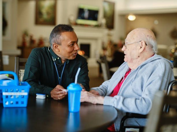 A man is talking to an elderly man in a wheelchair at a table.