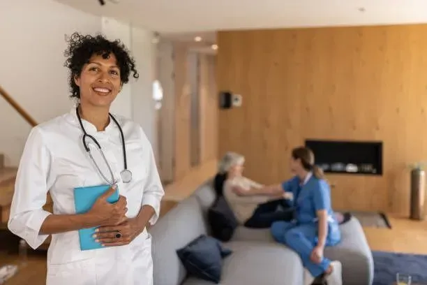 A nurse is standing in a living room holding a clipboard.