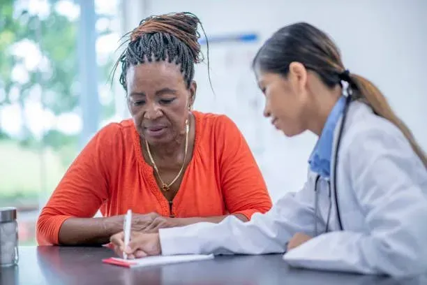 A doctor is talking to a patient who is writing on a piece of paper.