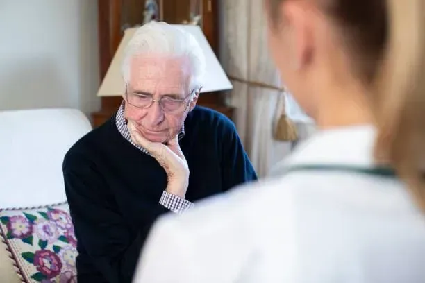 An elderly man is sitting on a couch talking to a doctor.