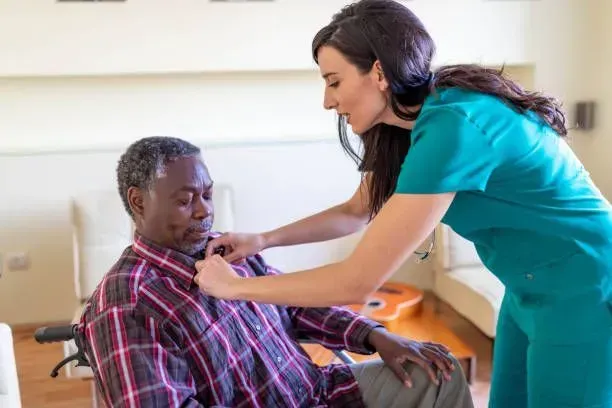 A nurse is helping an elderly man in a wheelchair with his tie.